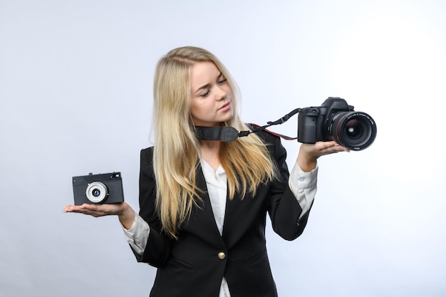 Jovem loira compara câmera de filme retrô e câmeras DSLR modernas em fundo branco