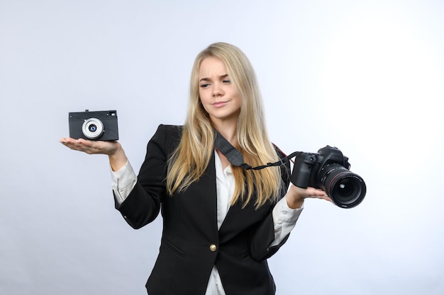 Jovem loira compara câmera de filme retrô e câmeras DSLR modernas em fundo branco