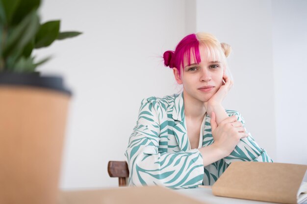 Jovem loira de cabelo rosa sentada à mesa no escritório e olhando para a câmera