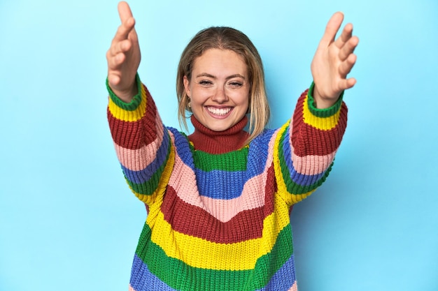 Jovem loira de camisola multicolor sente-se confiante dando um abraço à câmera