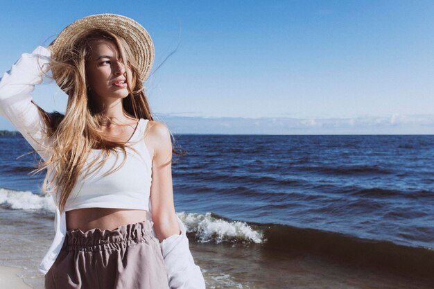 Jovem loira de chapéu na praia em um dia ensolarado