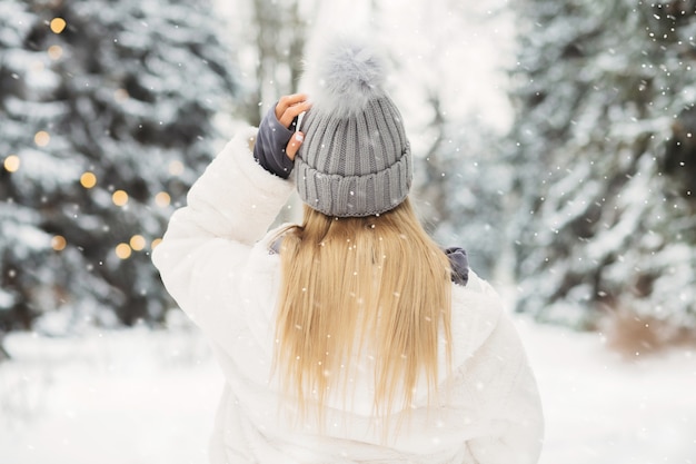 Jovem loira de jaleco branco olhando para a floresta em um clima de neve