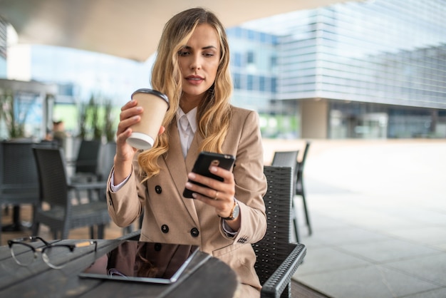 Jovem loira de negócios em uma pausa para o café usando seu smartphone