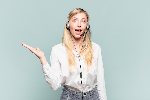 Jovem loira de telemarketing sentindo-se feliz, surpresa e alegre, sorrindo com atitude positiva, percebendo uma solução ou ideia