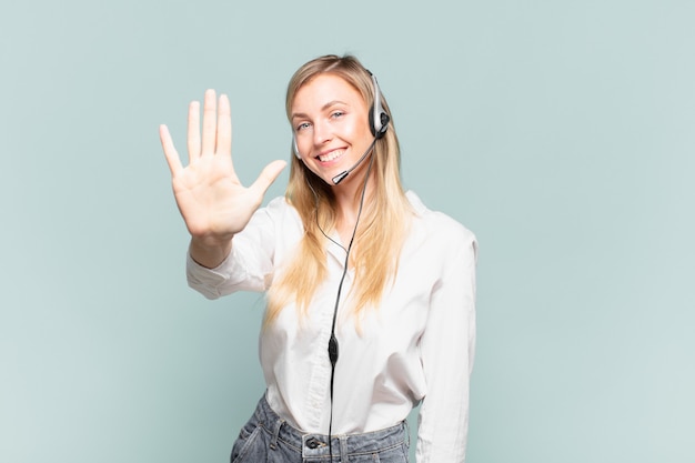 Jovem loira de telemarketing sorrindo e parecendo amigável, mostrando o número cinco ou quinto com a mão para a frente, em contagem regressiva