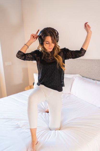 Foto jovem loira descalça caucasiana com fones de ouvido, dançando e curtindo música na cama