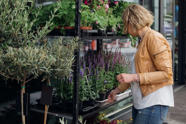 Jovem loira, dona de uma floricultura, corrige as plantas expostas na vitrine da rua. Pequenos negócios. Comércio de flores. Floricultura e jardinagem. Estilo de vida. Floricultura.