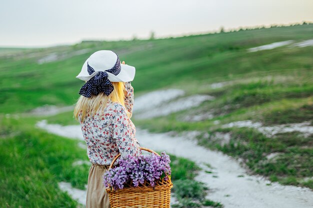 Jovem loira em um chapéu e com uma cesta de flores em um vestido