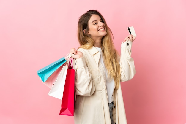 Jovem loira em um fundo isolado segurando sacolas de compras e um cartão de crédito