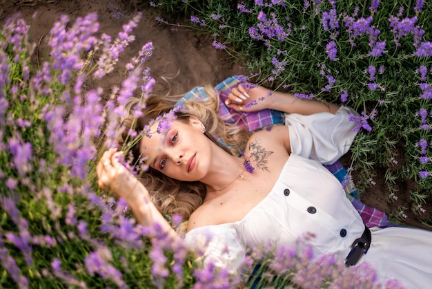 Foto jovem loira em um vestido branco deitada em flores de lavanda retrato de vista superior