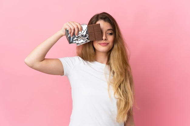 Jovem loira em uma parede isolada tomando uma pastilha de chocolate e surpresa