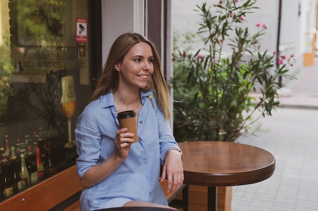 Jovem loira encantadora com café em um café de rua no verão