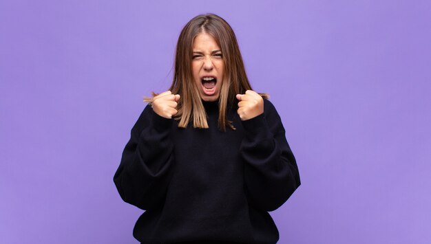 Jovem loira gritando agressivamente com olhar irritado, frustrado e irritado e punhos cerrados, sentindo-se furiosa