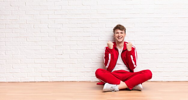 Jovem loira gritando triunfantemente, rindo e se sentindo feliz e animado enquanto comemorava o sucesso sentado no chão