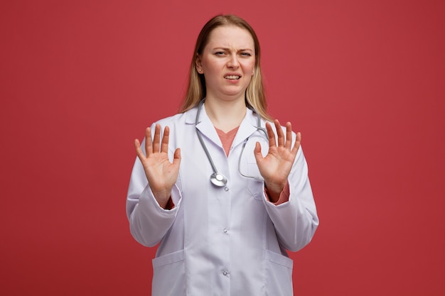 Jovem loira irritada com uma médica usando um manto médico e um estetoscópio pendurado no pescoço, fazendo um gesto de recusa