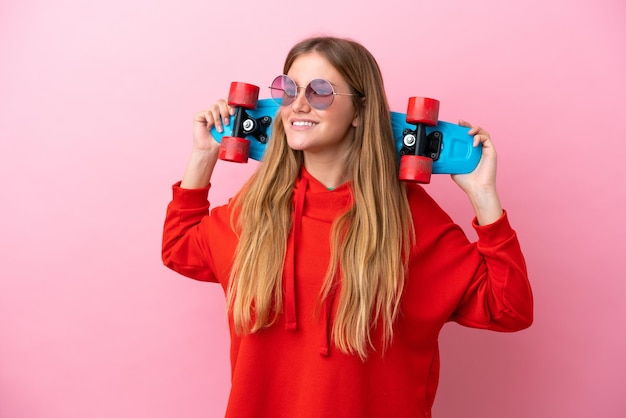 Jovem loira isolada em fundo rosa com um skate com expressão feliz