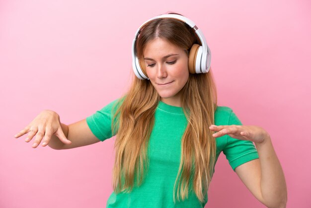 Jovem loira isolada em fundo rosa ouvindo música e dançando