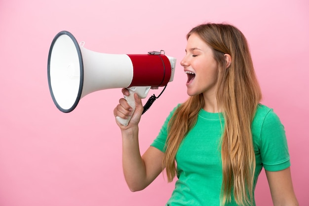 Jovem loira isolada em um fundo rosa gritando em um megafone para anunciar algo em posição lateral