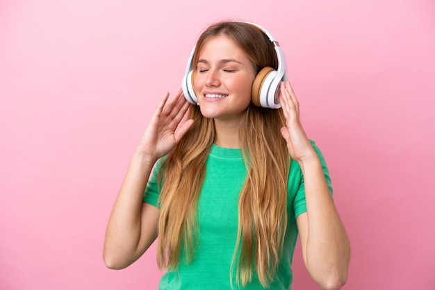 Jovem loira isolada em um fundo rosa ouvindo música e cantando