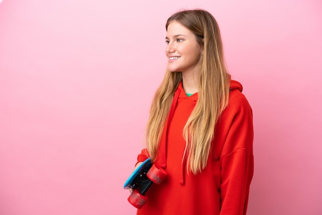 Jovem loira isolada no fundo rosa com um skate