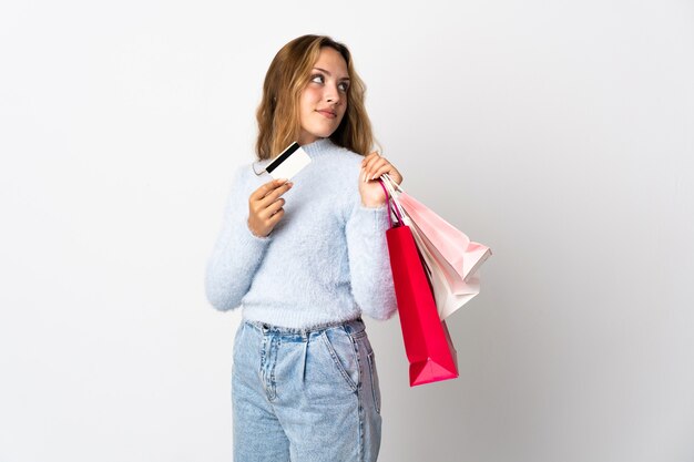 Jovem loira isolada segurando sacolas de compras e um cartão de crédito e pensando