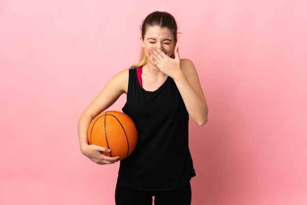 Jovem loira jogando basquete isolada no espaço rosa feliz e sorridente cobrindo a boca com a mão