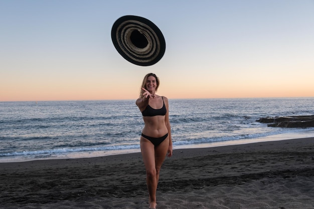 Jovem loira jogando chapéu ao pôr do sol