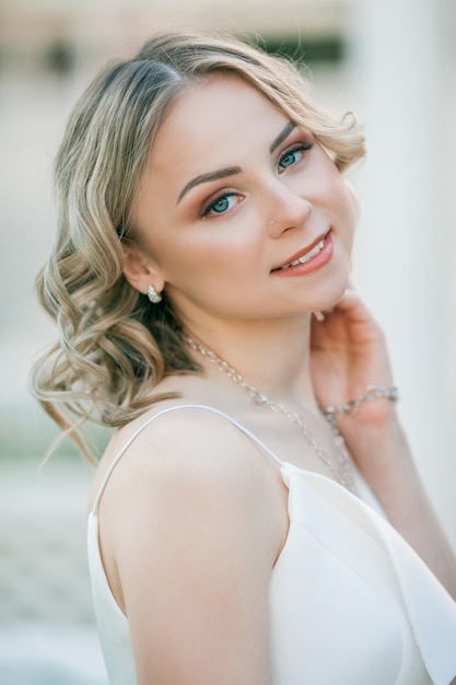 Jovem loira linda de 20 anos com cabelos cacheados em um vestido branco nos raios ensolarados do sol no parque Um modelo elegante caminha pelo parque florescente da cidade no verão