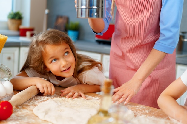 Jovem loira, mãe e filhos se divertindo enquanto cozinham massa de perto