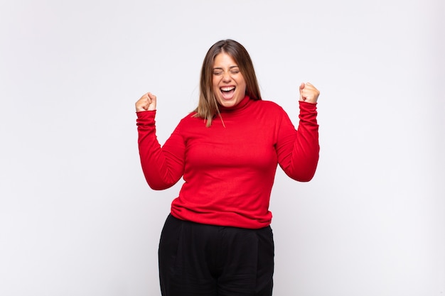 Jovem loira parecendo extremamente feliz e surpresa, comemorando o sucesso, gritando e pulando