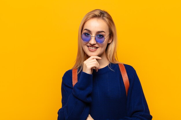 Jovem loira parecendo feliz e sorrindo com a mão no queixo, pensando ou fazendo uma pergunta, comparando opções