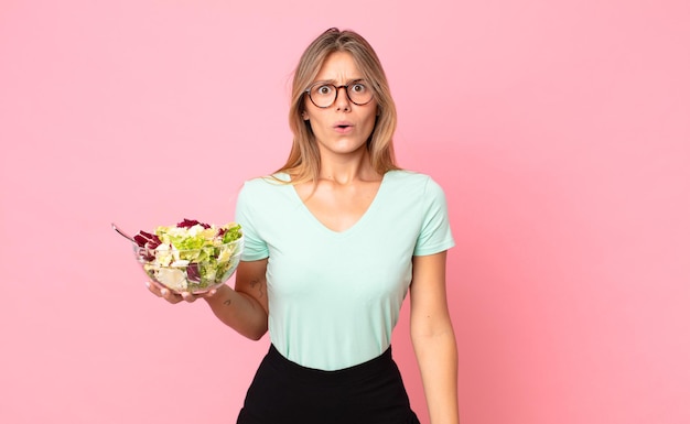 Jovem loira parecendo muito chocada ou surpresa e segurando uma salada