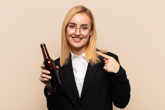 jovem loira parecendo orgulhosa, confiante e feliz, sorrindo e apontando para si mesma ou fazendo o primeiro sinal