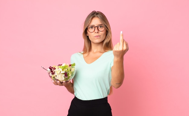 Jovem loira se sentindo irritada, irritada, rebelde e agressiva segurando uma salada