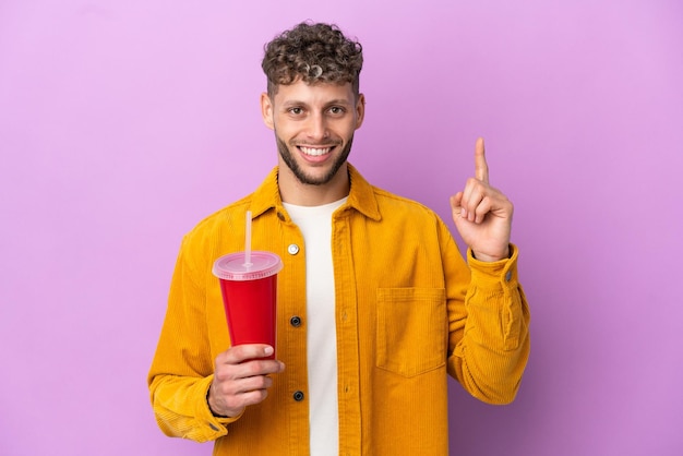 Jovem loira segurando refrigerante isolado no fundo roxo apontando uma ótima ideia