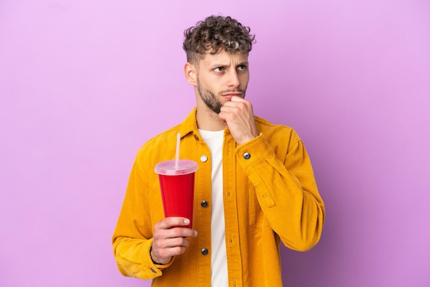 Jovem loira segurando refrigerante isolado no fundo roxo e olhando para cima