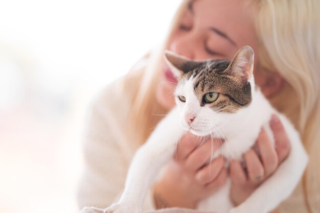 Jovem loira segurando um gato branco em um fundo bem iluminado