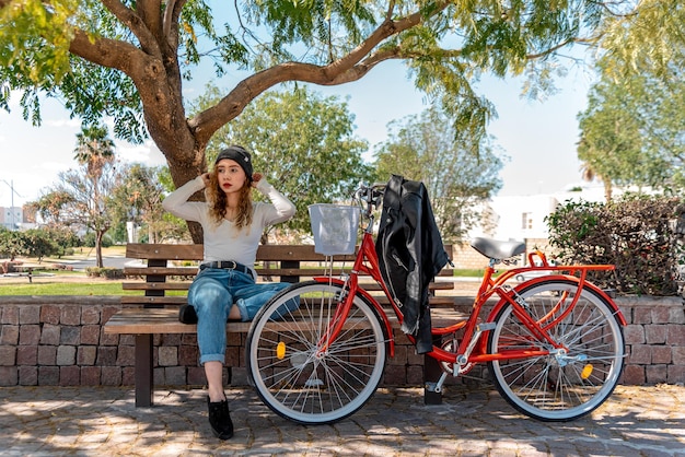 Jovem loira sentada em um banco, descansando no parque com sua bicicleta