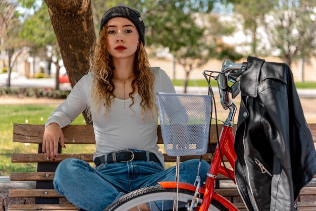 Jovem loira sentada em um banco, descansando no parque com sua bicicleta