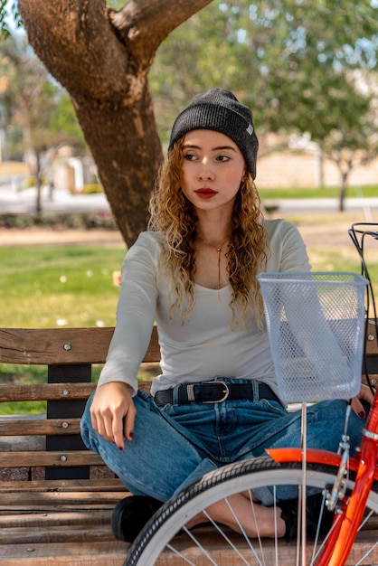 Jovem loira sentada em um banco, descansando no parque com sua bicicleta