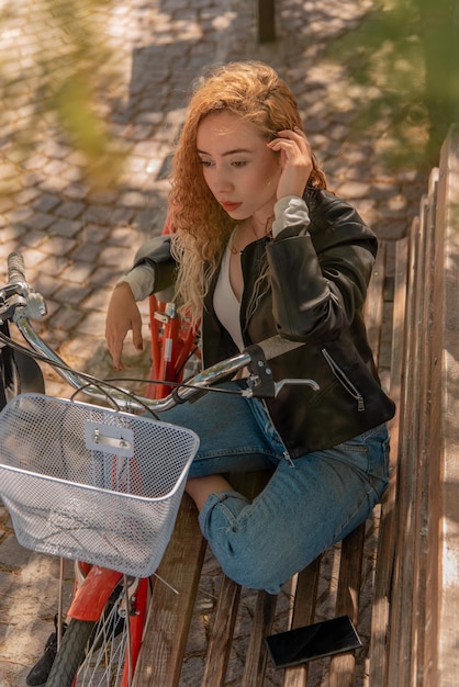 Jovem loira sentada em um banco, descansando no parque com sua bicicleta