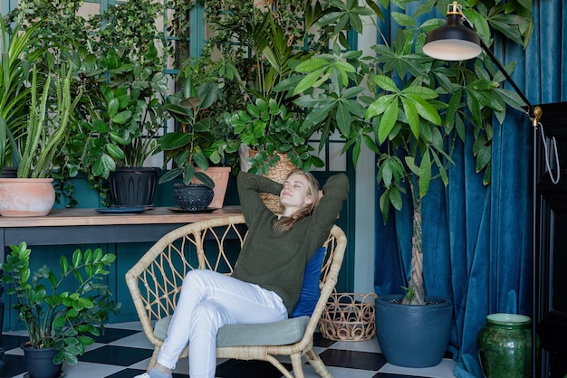 Jovem loira sentada em uma cadeira confortável rodeada de plantas