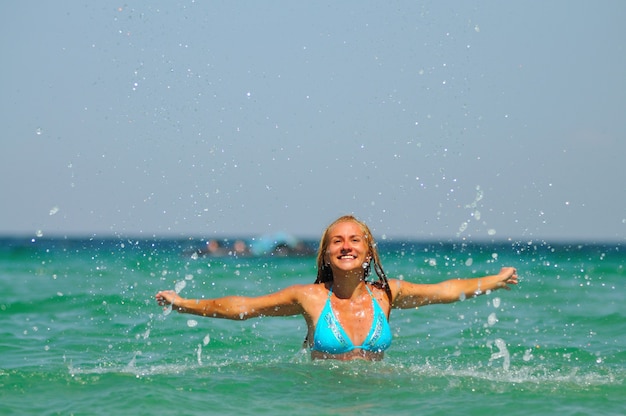 Jovem loira sorridente de biquíni azul em pé e curtindo estar na água em um dia claro de verão ensolarado. Conceito de felicidade, férias e liberdade