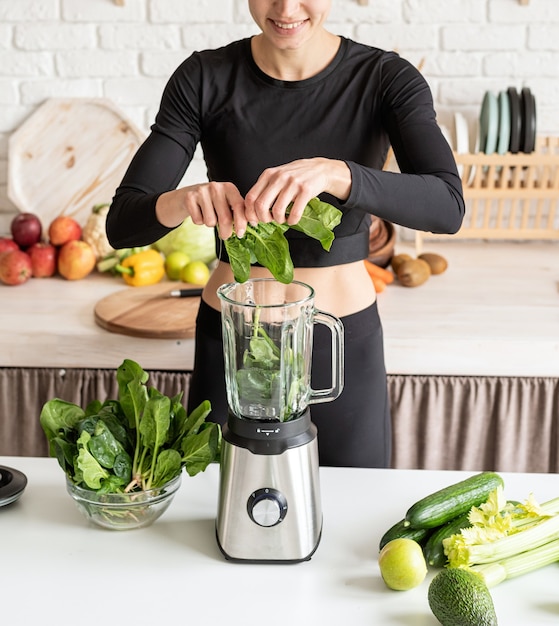 Foto jovem loira sorridente fazendo suco verde na cozinha de casa