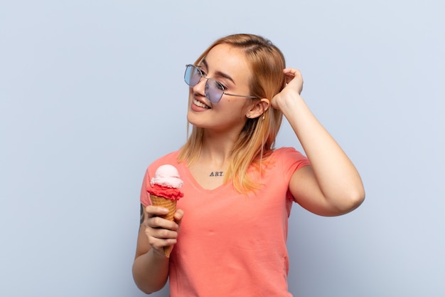 Foto jovem loira sorrindo alegre e casualmente, levando a mão na cabeça com um olhar positivo, feliz e confiante