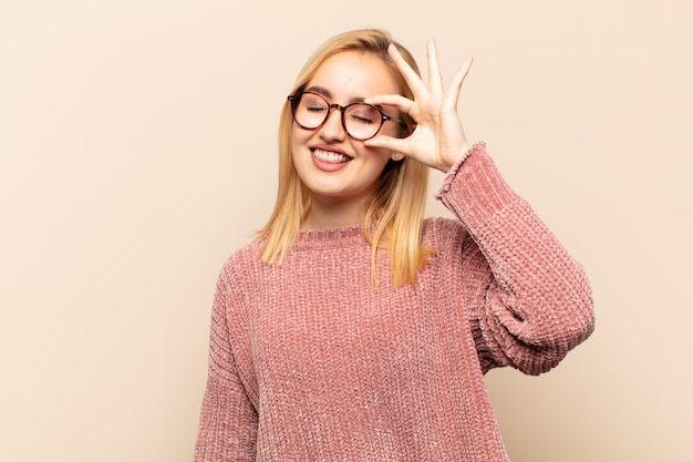 Jovem loira sorrindo alegremente com uma careta engraçada, brincando e olhando pelo olho mágico, espionando segredos