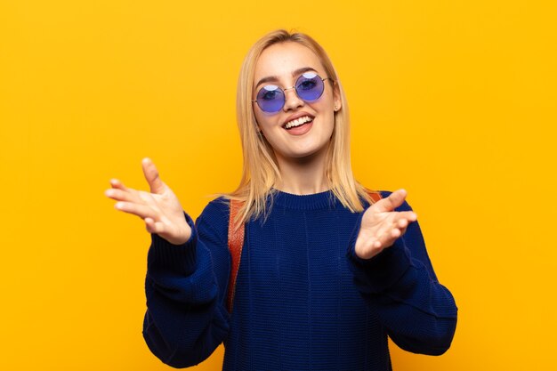 Jovem loira sorrindo alegremente dando um abraço caloroso, amigável e afetuoso de boas-vindas, sentindo-se feliz e adorável