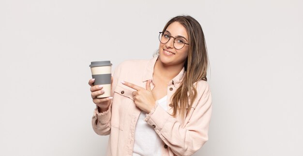 Jovem loira sorrindo alegremente, sentindo-se feliz e apontando para os lados e para cima, mostrando o objeto no espaço da cópia