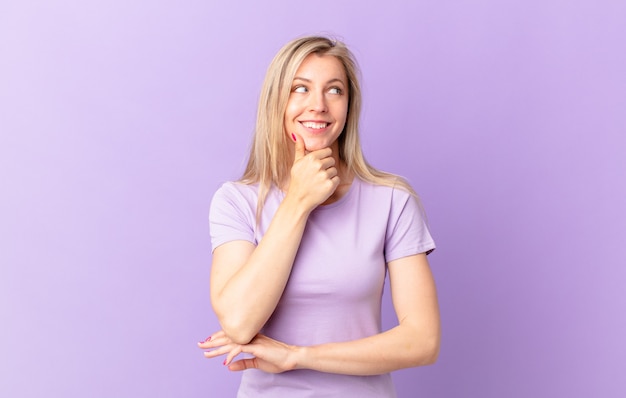 Jovem loira sorrindo com uma expressão feliz e confiante com a mão no queixo