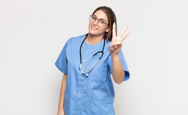 Jovem loira sorrindo e parecendo amigável, mostrando o número três ou terceiro com a mão para a frente